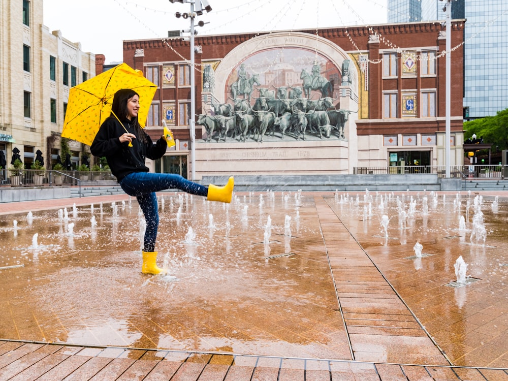 person in blue denim jeans and yellow umbrella walking on street during daytime