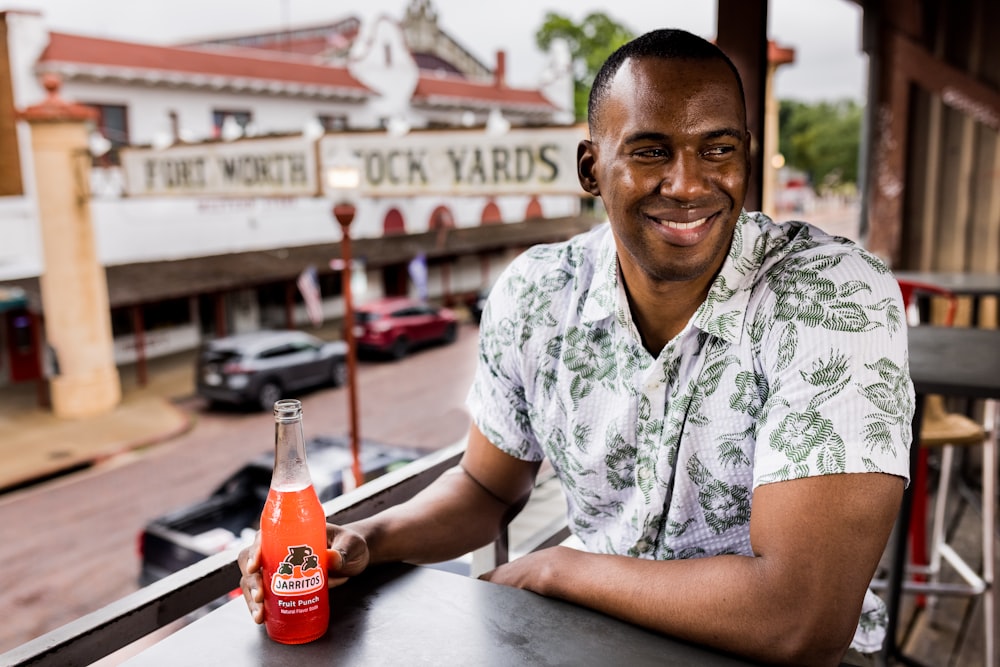 man in white and green floral button up shirt sitting beside table with coca cola bottle