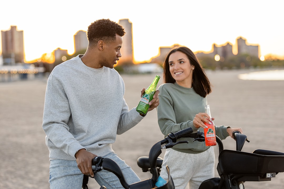 man in white sweater holding green bottle beside woman in white sweater riding on bicycle