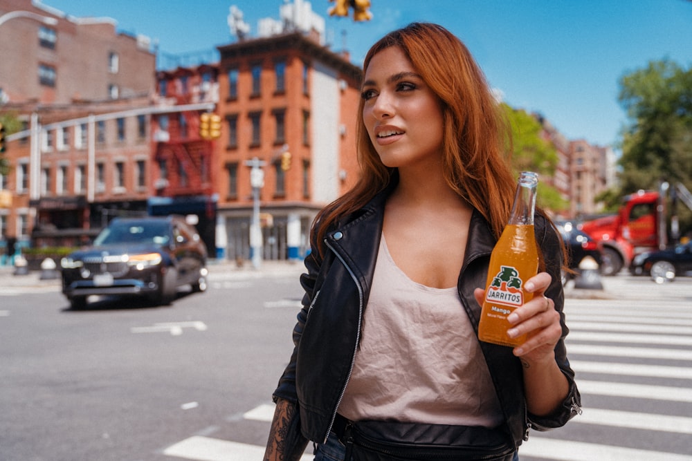 woman in white shirt and black leather jacket holding orange bottle