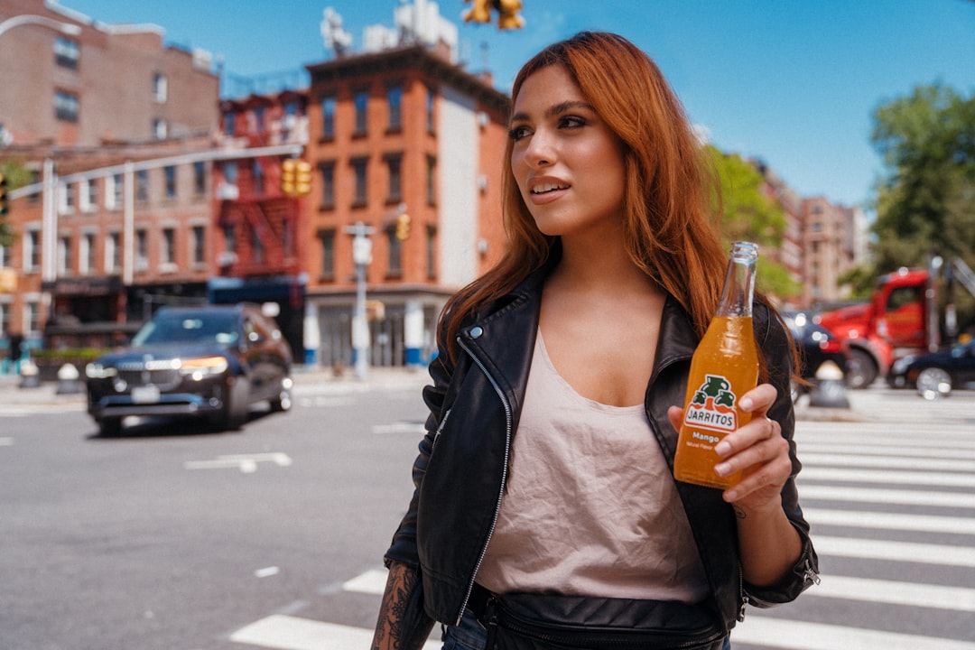 woman in white shirt and black leather jacket holding orange bottle, Jarritos Mango explores the City