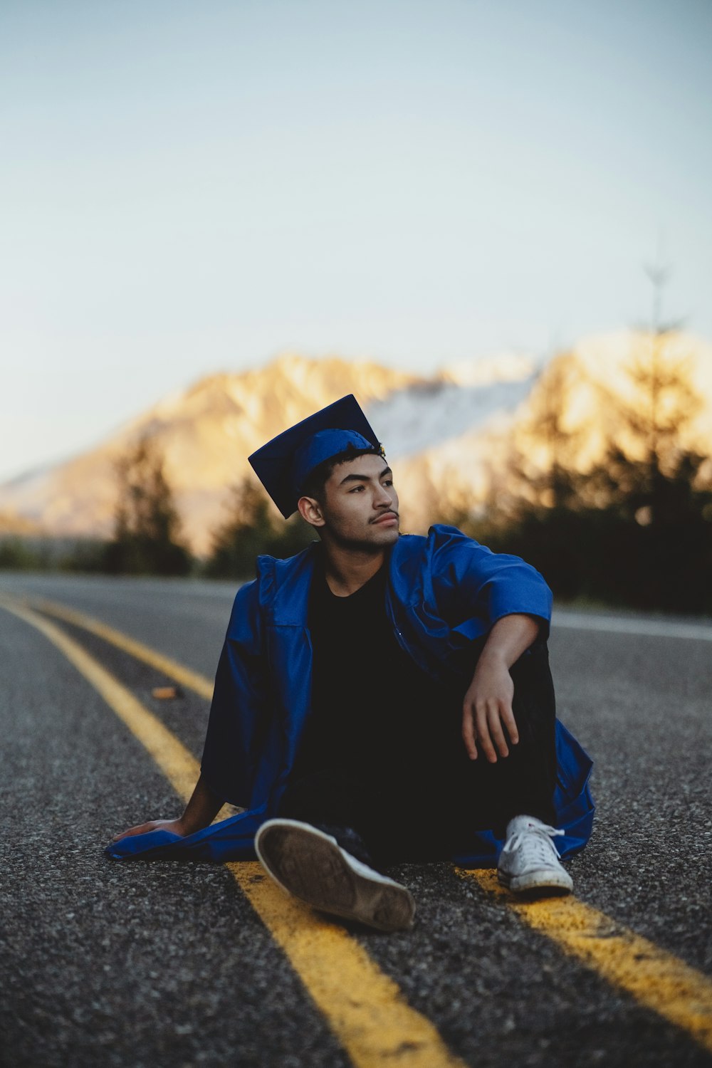 man in blue jacket and black pants sitting on road during daytime