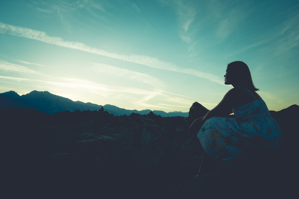 silhouette of woman sitting on rock during daytime