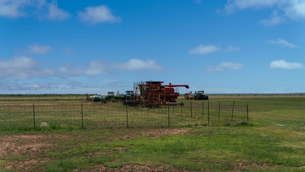 Wide shot of a rural farm landscape with tractors and crops under a clear sky.