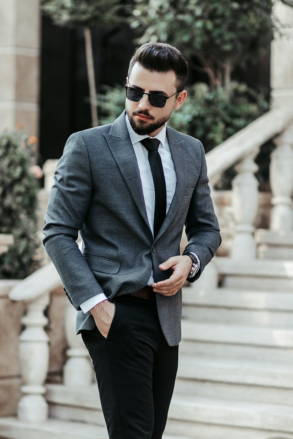 man in gray suit jacket and black pants wearing black sunglasses standing on gray concrete stairs