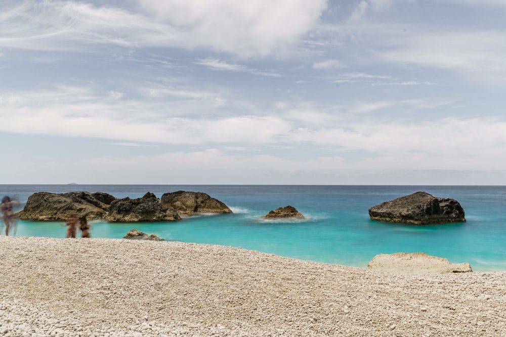 brauner Sandstrand mit Felsen unter weißen Wolken und blauem Himmel tagsüber