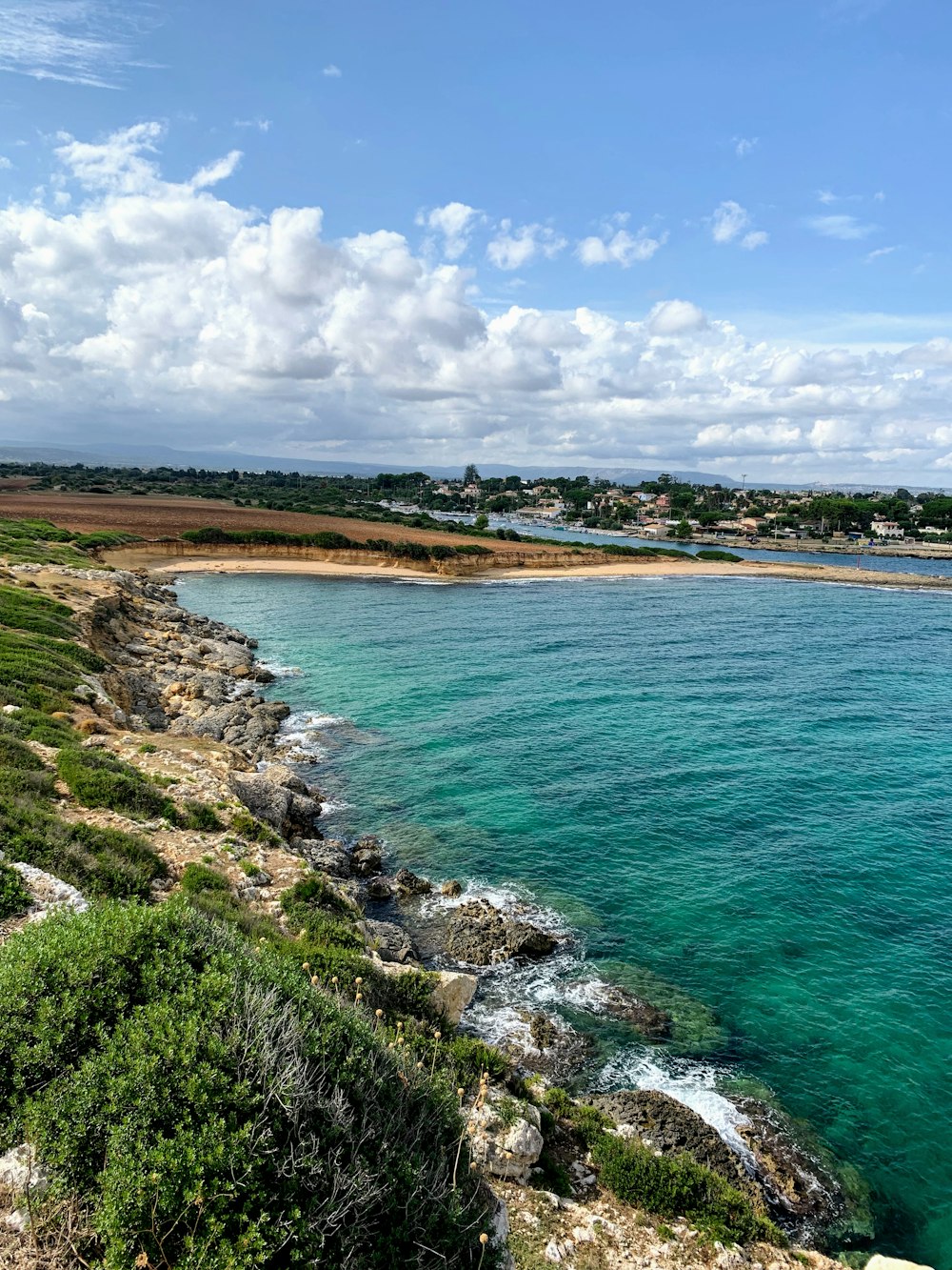 campo di erba verde vicino allo specchio d'acqua sotto il cielo nuvoloso blu e bianco durante il giorno