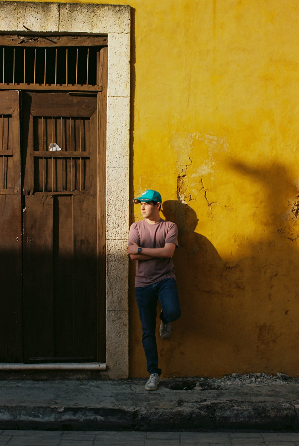 homem em boné azul e camiseta marrom apoiando-se na porta de madeira marrom