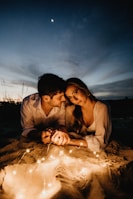 Couple enjoying a candlelit dinner on a sandy beach under soft lantern light.