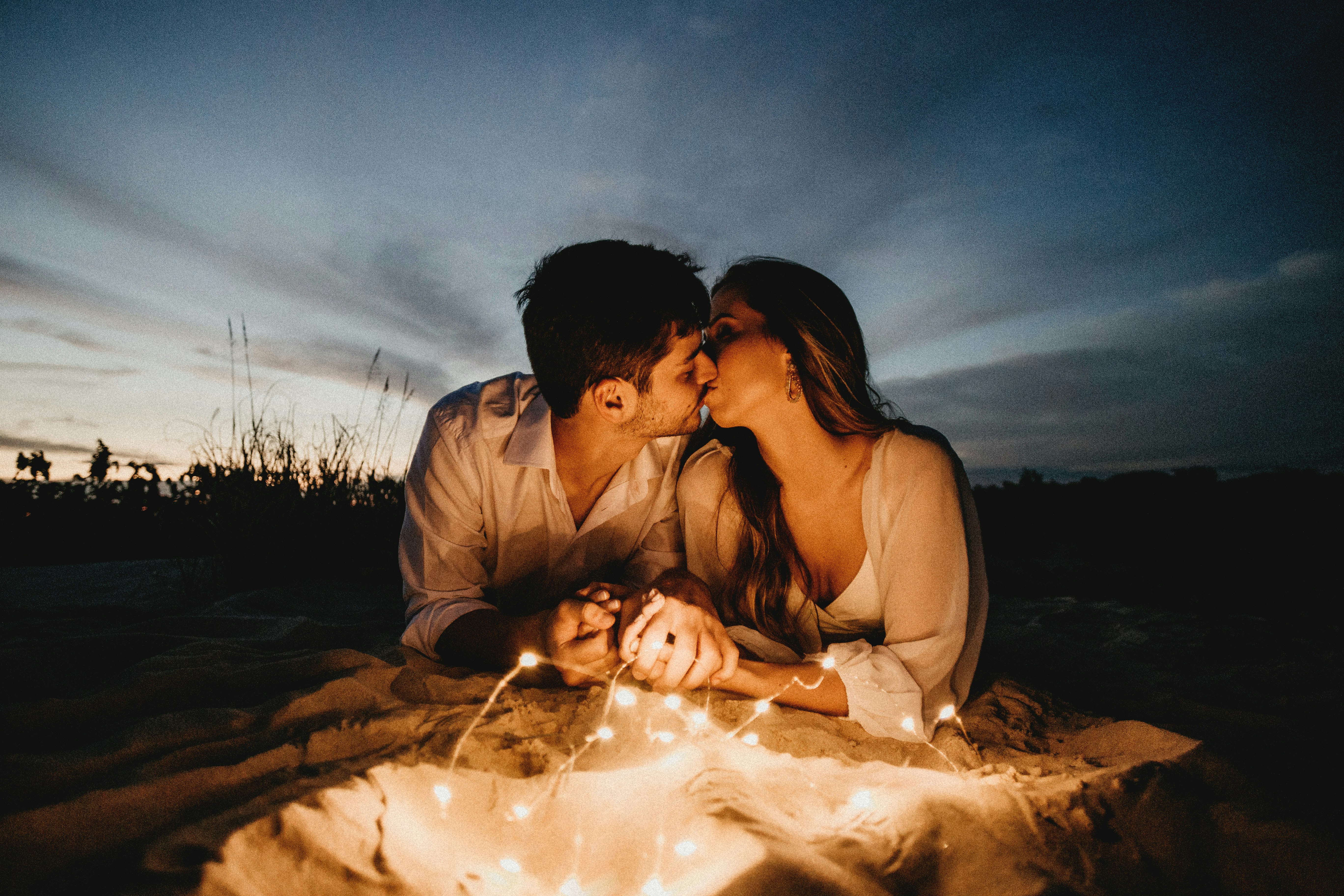 man and woman kissing on brown sand during night time