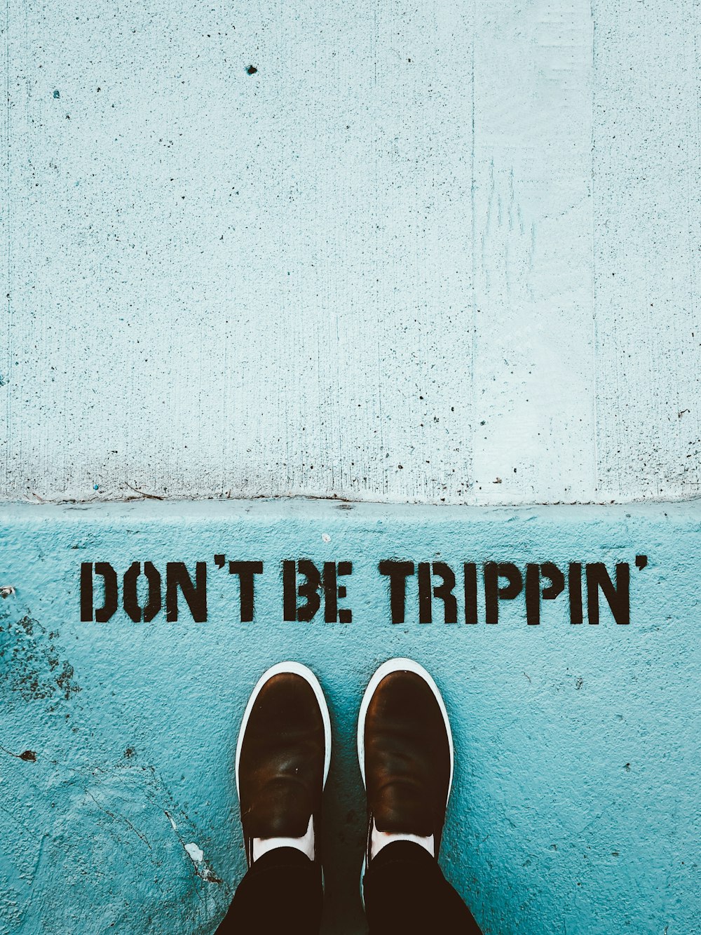 person in brown shoes standing on gray concrete wall with no smoking sign