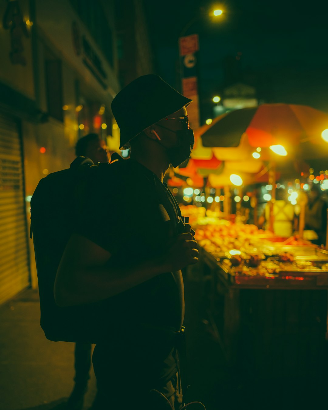 man in black shirt and black cap standing in front of food stall during night time