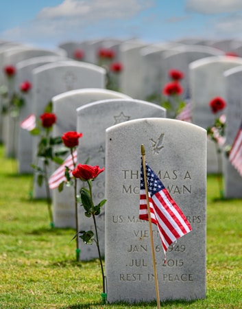 Rows of white marble headstones decorated with red roses and small American flags at a national cemetery