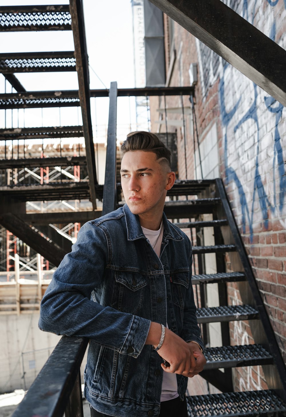 man in blue denim button up jacket standing near brown metal ladder during daytime