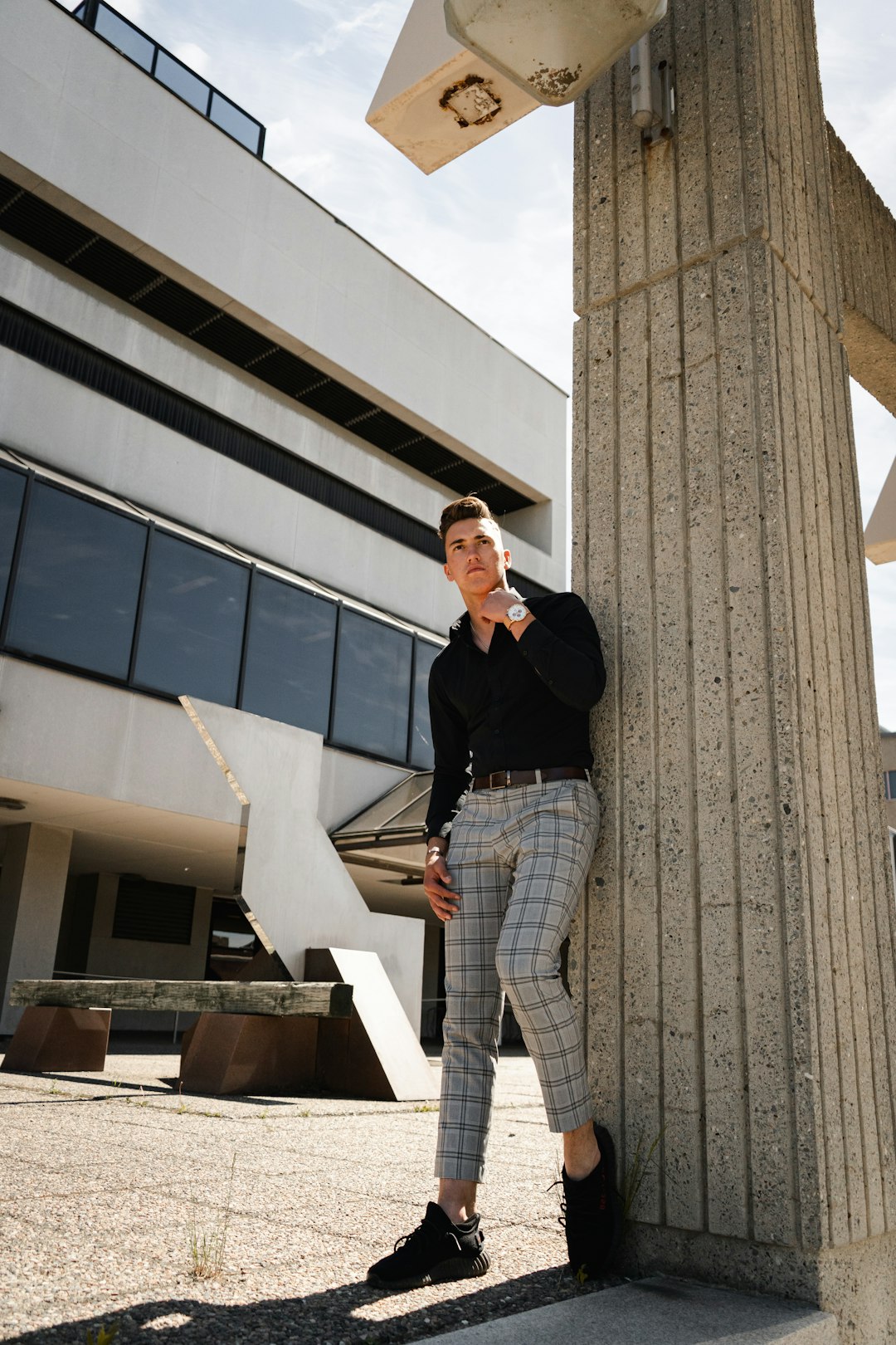 woman in black blazer and white and black plaid pants standing beside brown concrete building during