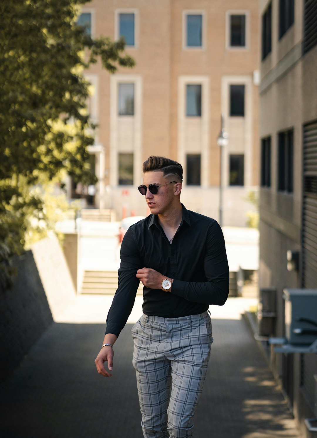 man in black dress shirt and gray plaid shorts standing on sidewalk during daytime