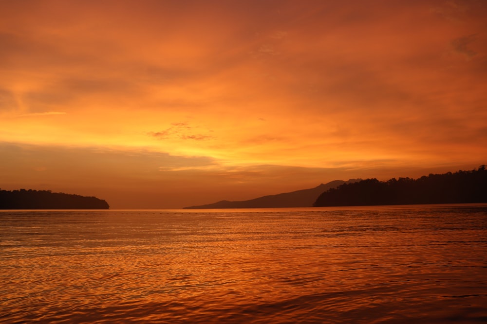 silhouette of mountain beside sea during sunset