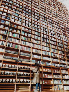 man in brown coat standing in front of brown wooden book shelf
