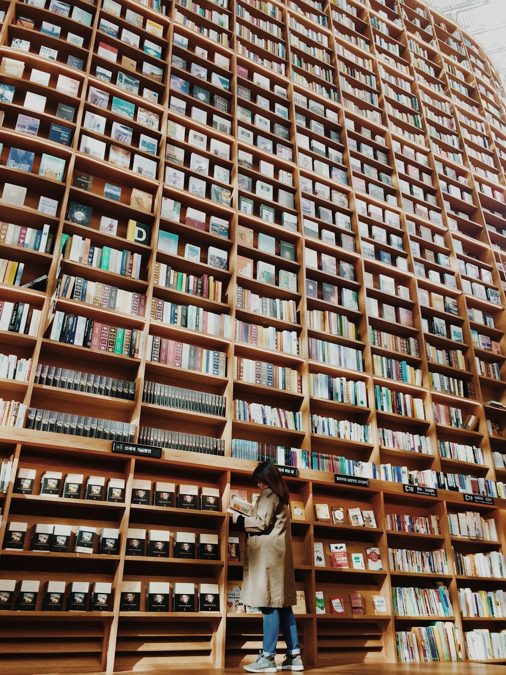 man in brown coat standing in front of brown wooden book shelf