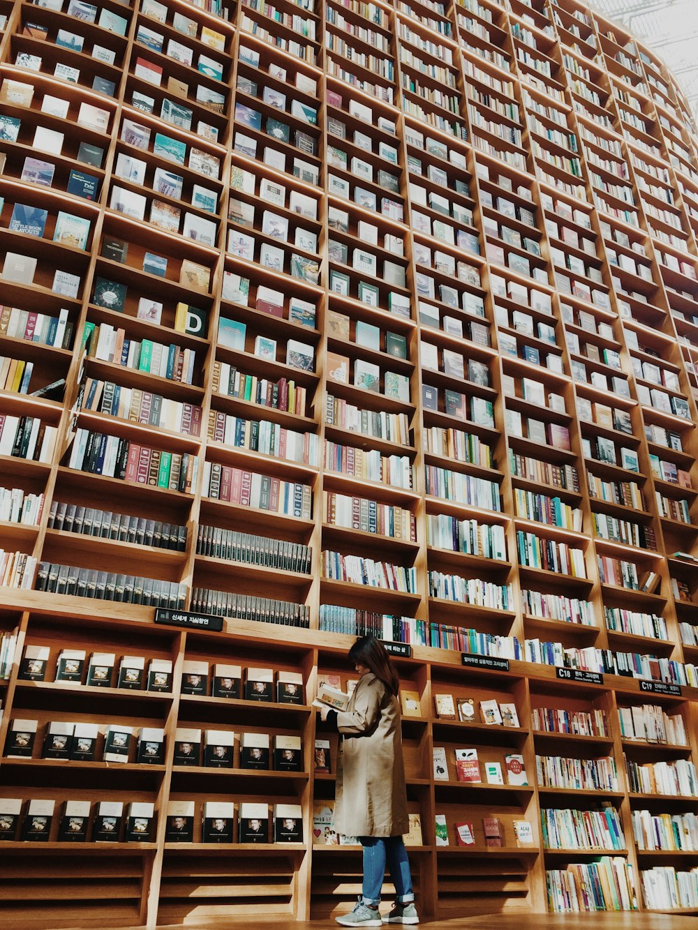 hombre en abrigo marrón de pie frente a estante de libros de madera marrón