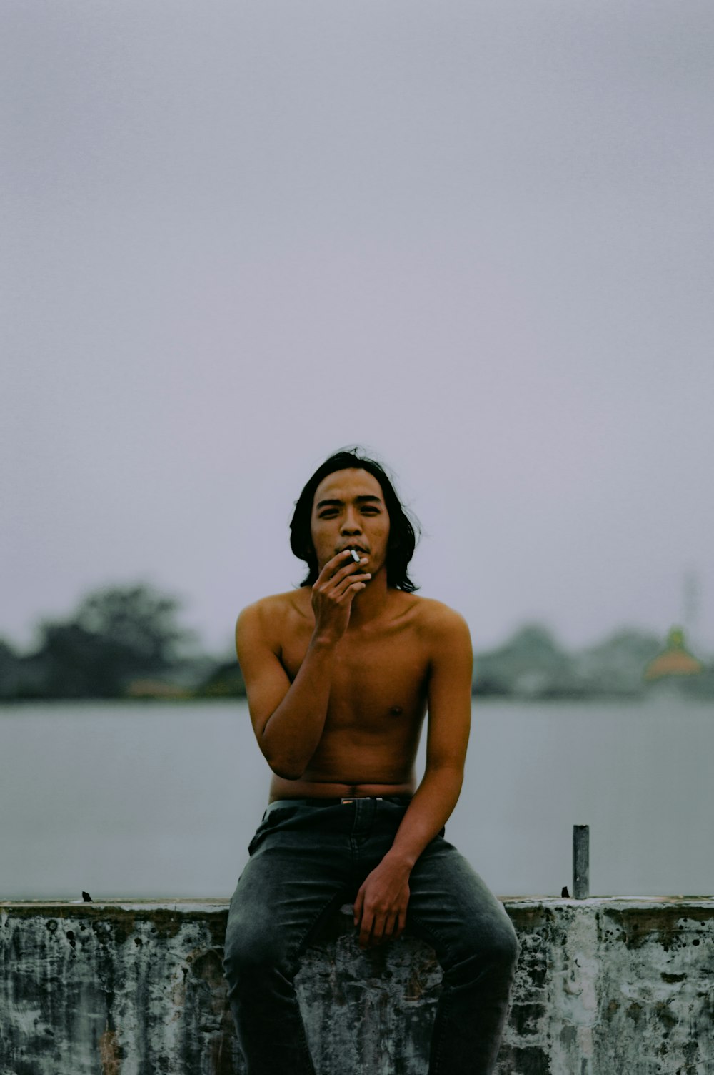 topless man in blue denim jeans sitting on wooden railings during daytime