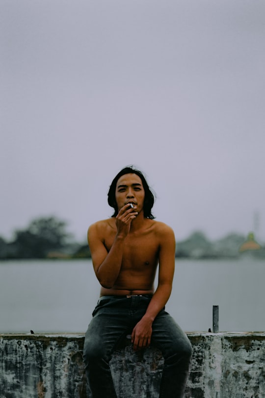 topless man in blue denim jeans sitting on wooden railings during daytime in Malang Indonesia