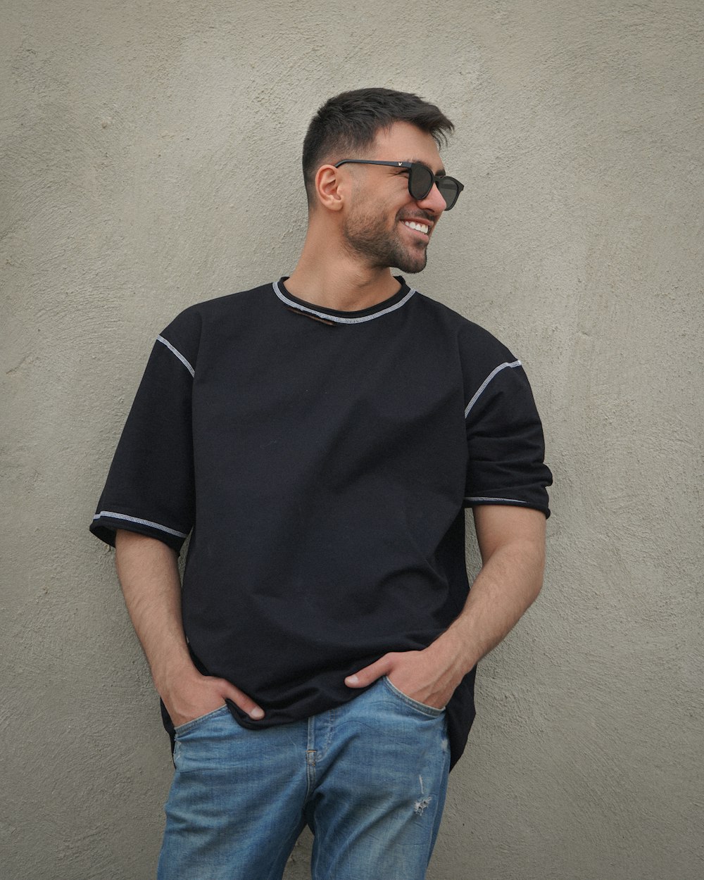 man in black crew neck t-shirt and blue denim jeans standing beside white wall