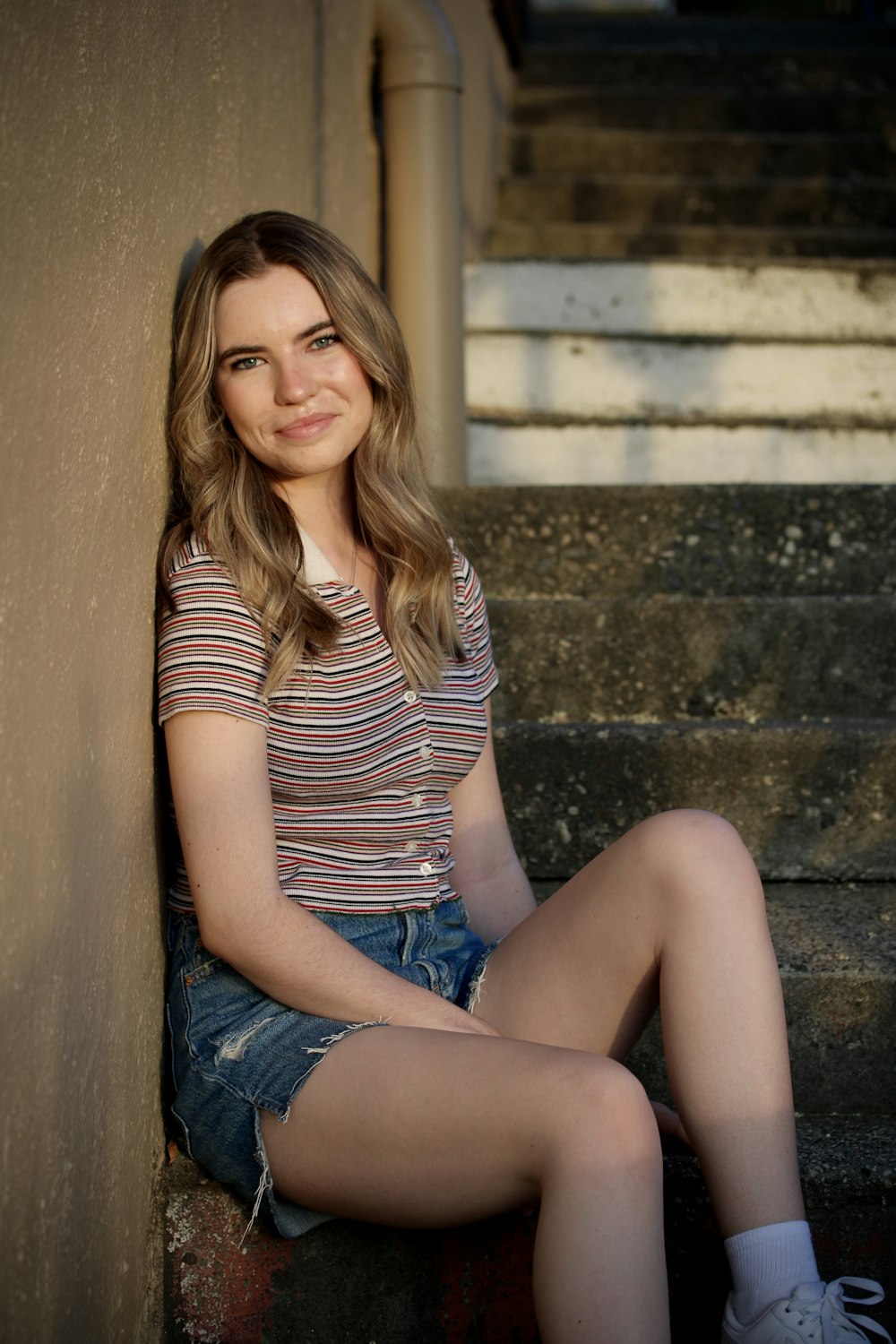 woman in black and white striped shirt and blue denim shorts sitting on concrete stairs