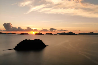 silhouette of island on body of water during sunset