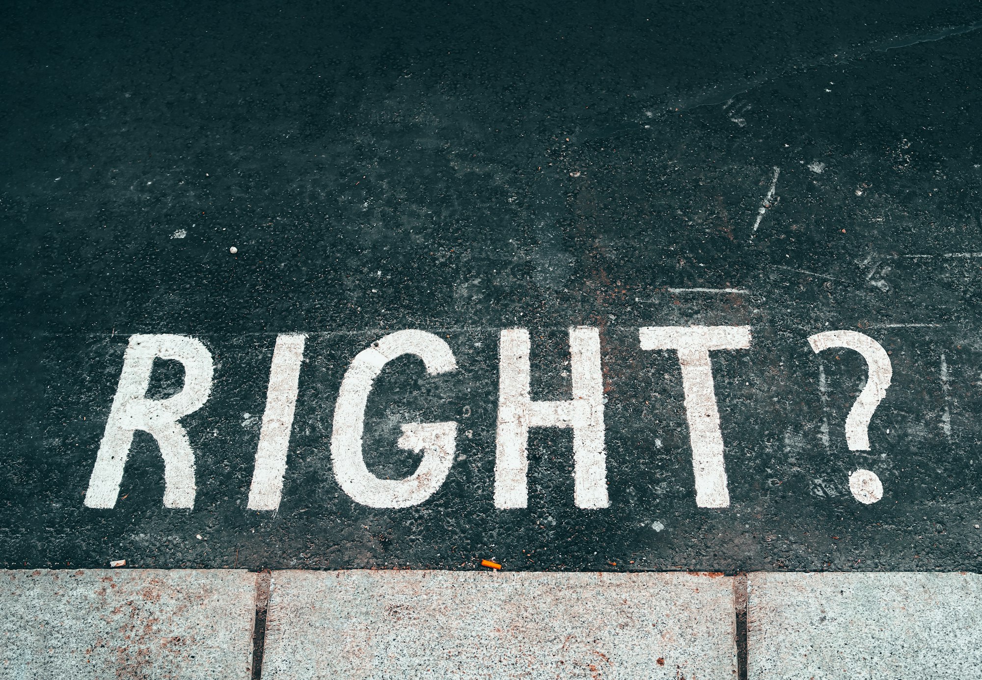 the word "right?" painted on asphalt next to a sidewalk