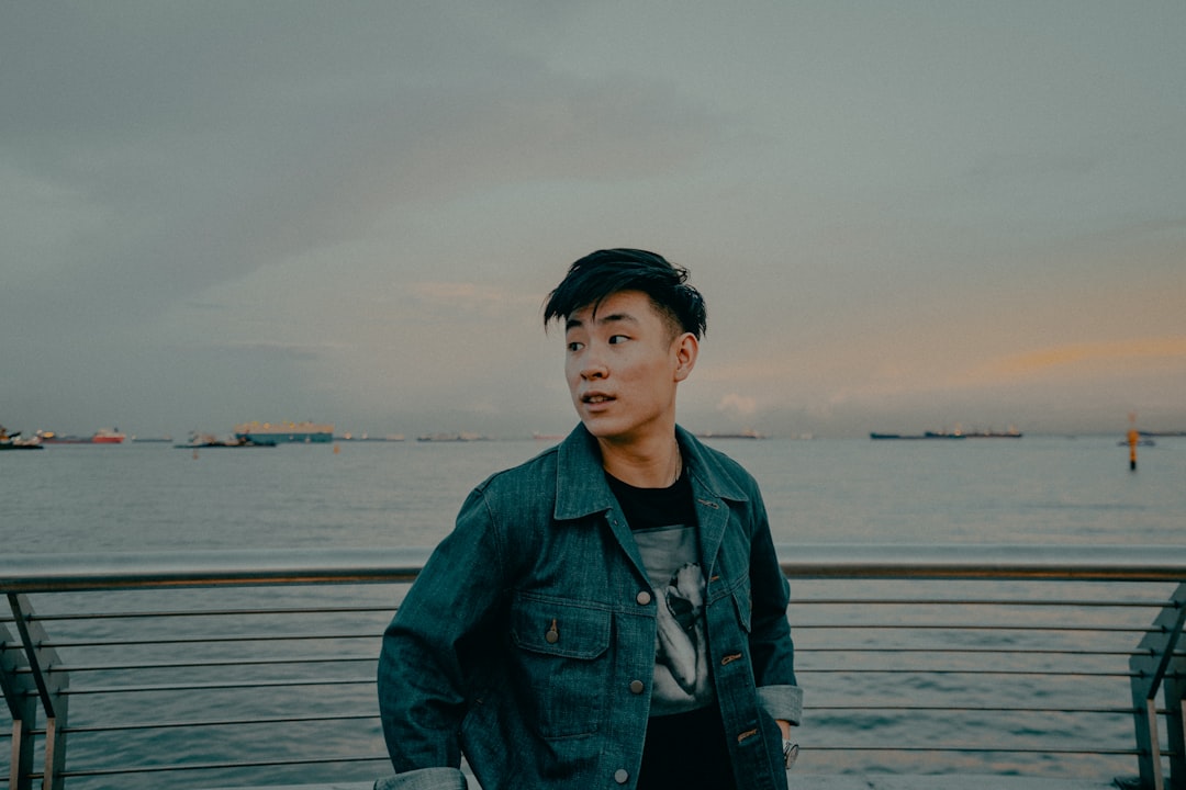 man in blue denim jacket standing on sea shore during daytime