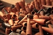 A pile of clay smoking pipes in various shades of brown and black, arranged haphazardly. The pipes are predominantly conical and cylindrical in shape, with some showing decorative markings.