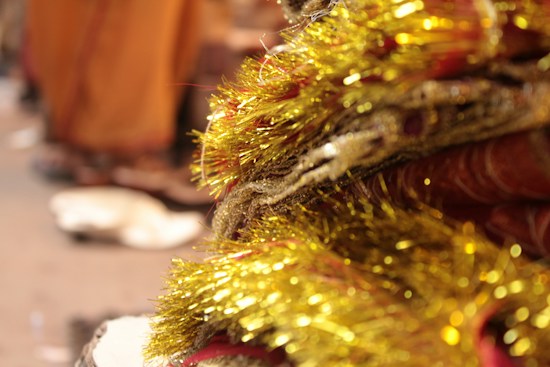A close-up of shimmering golden tinsel intertwined with rich red fabric, creating a festive and opulent appearance. The background is softly blurred, emphasizing the sparkling textures and warm hues.