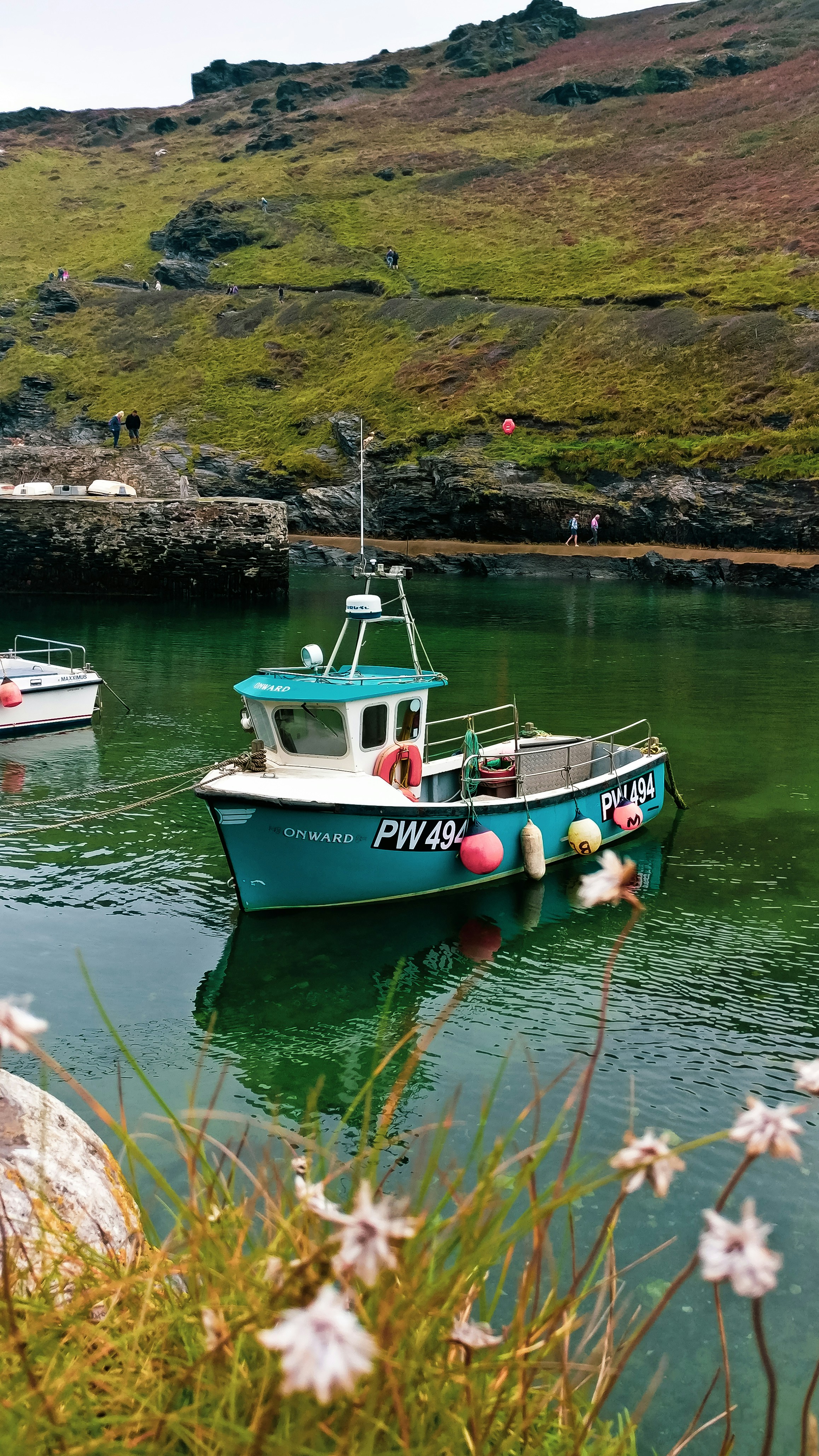 Small fishing vessel on calm teal waters of a coastal bay with rocky shoreline behind