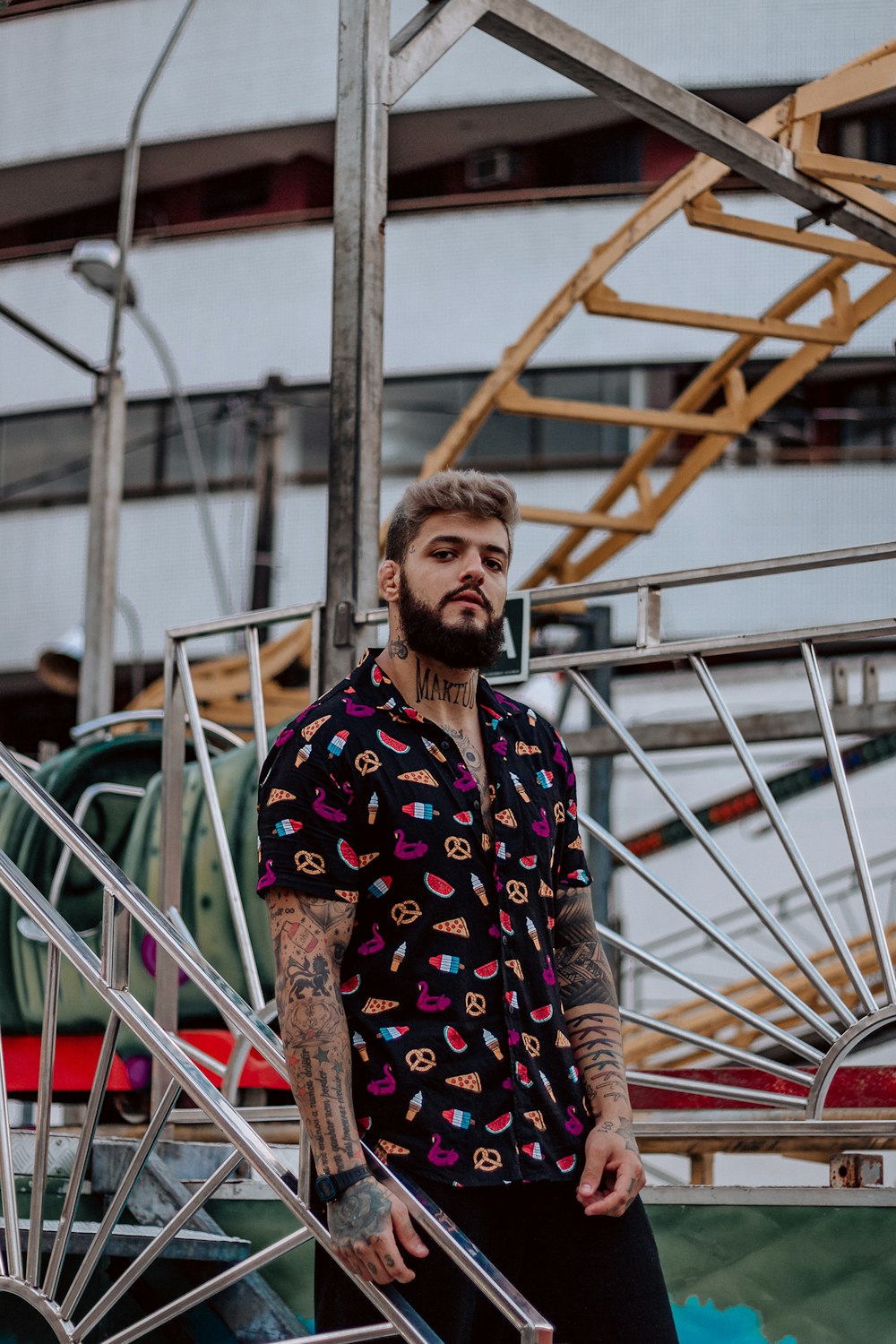 man in black and yellow floral dress shirt standing near white metal railings during daytime