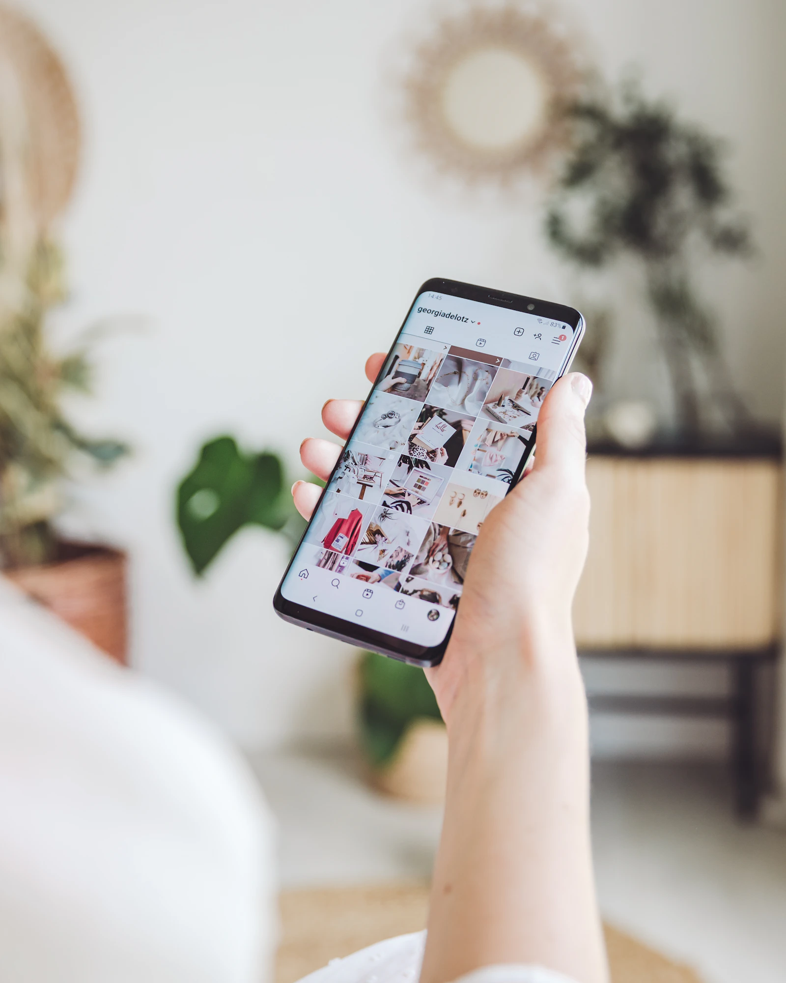 A phone held in one hand showing a grid of photo posts