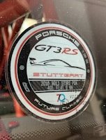 A circular decal featuring the Porsche logo, with text indicating the model GT3 RS and details like 'Stuttgart', '2016 9911 GT3RS PDK', and '4.0L Flat 6 NA'. The design includes black, white, and red colors with a graphic of a car silhouette and the words 'Future Classic'.