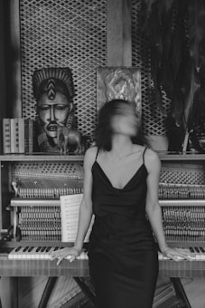 A woman in a dark dress sits on the edge of an open piano, with blurred motion in her face, surrounded by cultural artifacts and books, creating an artistic and mysterious atmosphere.