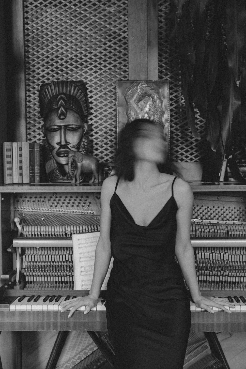 woman in black spaghetti strap dress standing beside piano