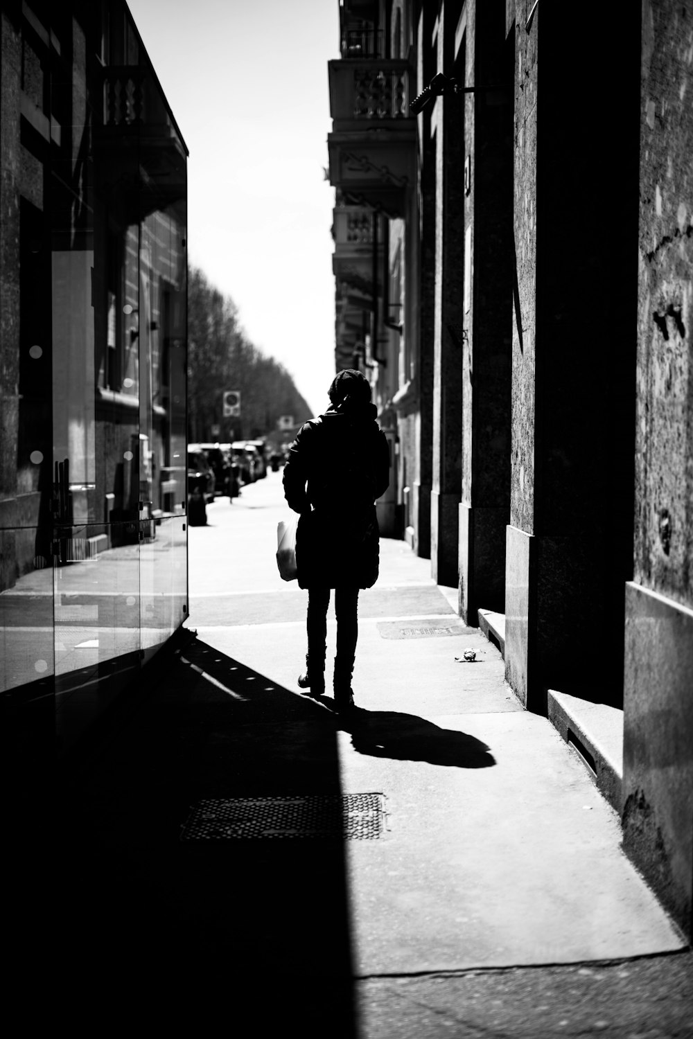 grayscale photo of woman walking on sidewalk
