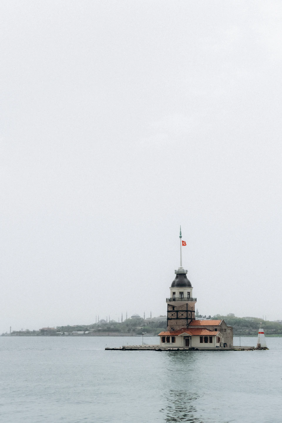 Bosphorus Tower stands tall against an overcast sky with a Turkish flag flying nearby