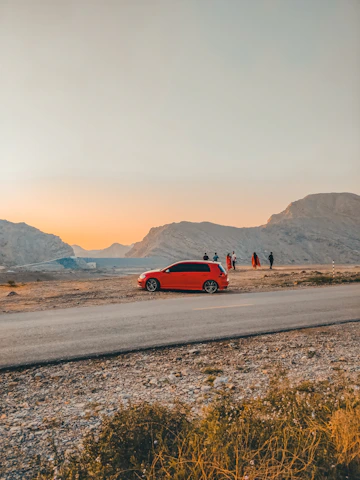 A vibrant photo of a shiny red car parked on a scenic mountain road during sunset.