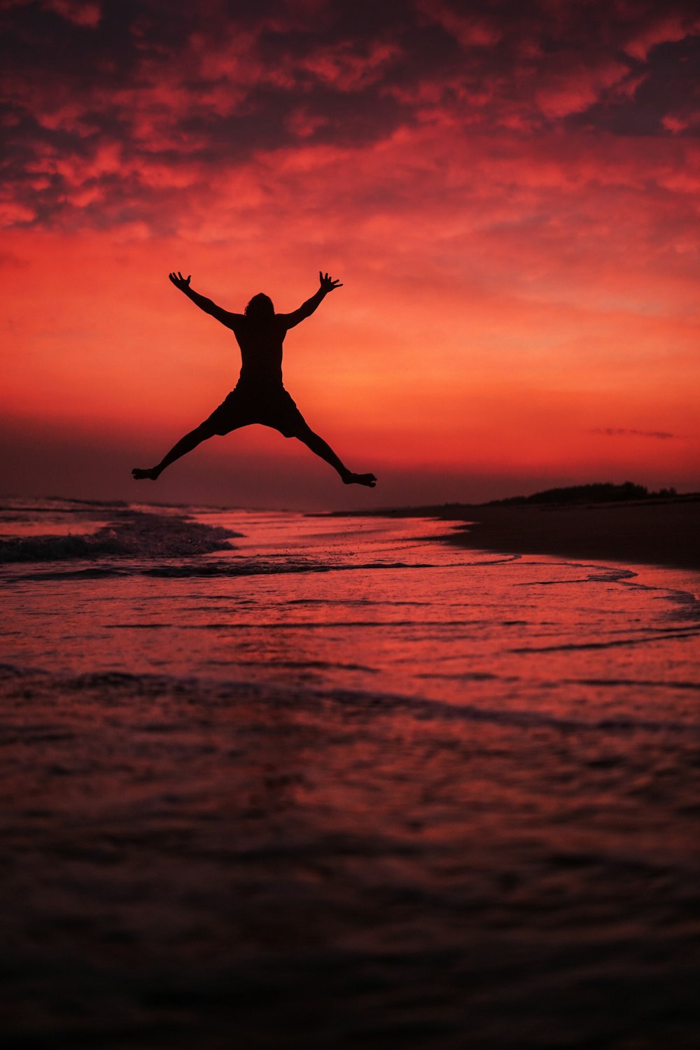 Silueta de mujer saltando en la playa durante la puesta del sol