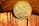 A gold-colored coin is placed against a background that appears to be wooden. The coin has intricate designs and the inscriptions 'CARDANO', 'SECURE LAYERED SMART CONTRACTS', and 'ADA' can be seen.