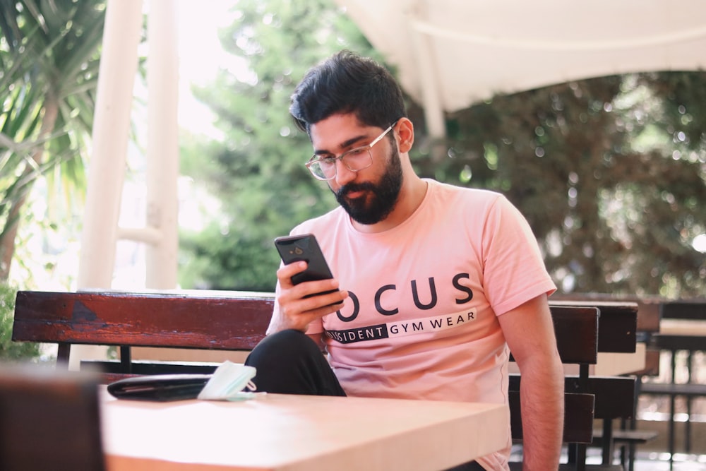 man in pink crew neck t-shirt sitting on brown wooden bench during daytime