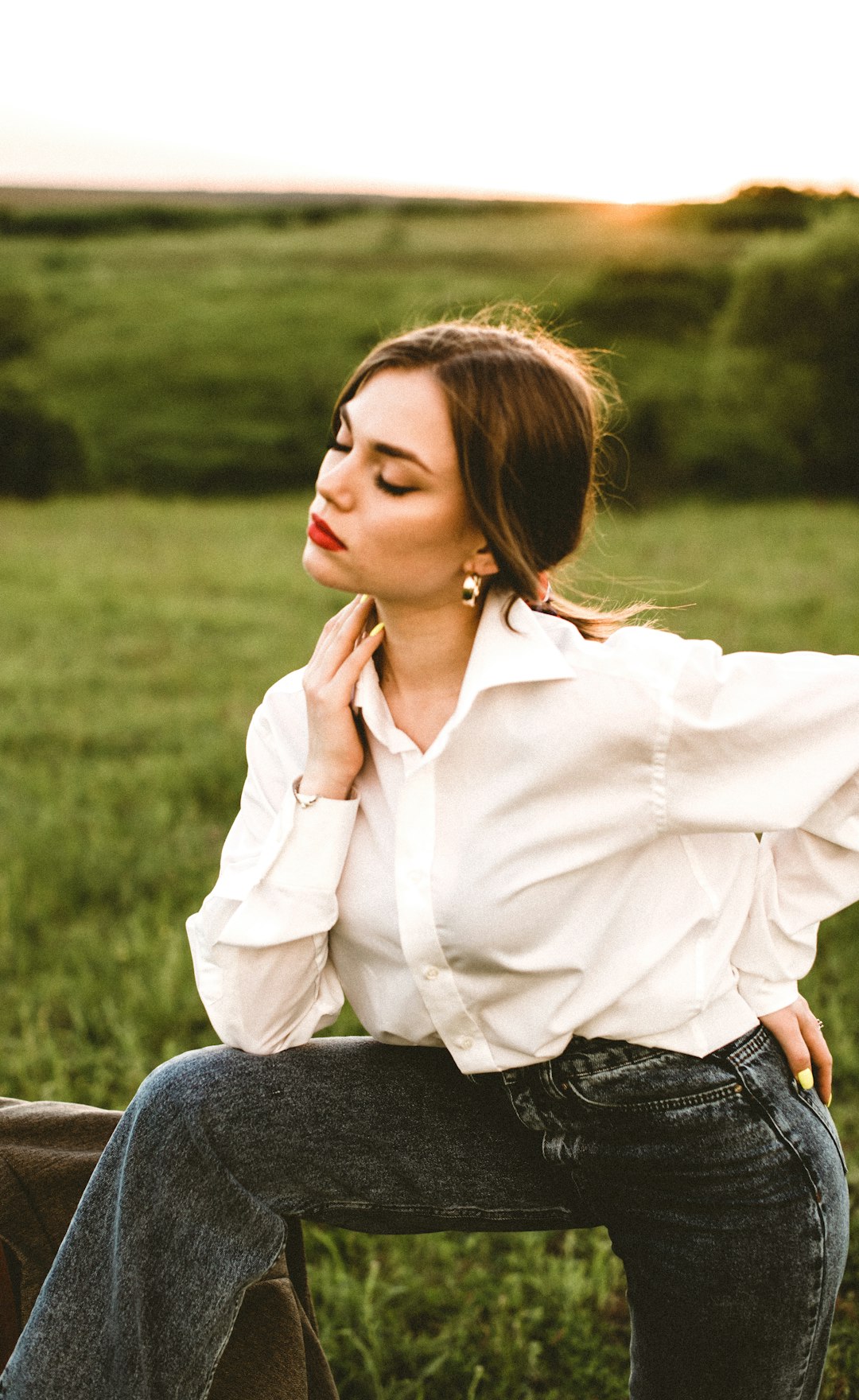 woman in white dress shirt and blue denim jeans sitting on grass field during daytime