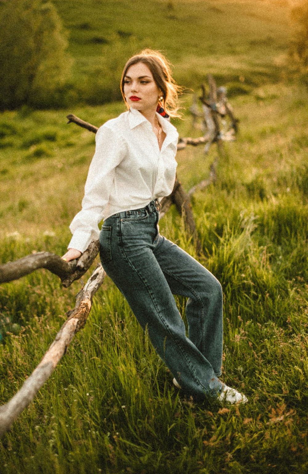 woman in white long sleeve shirt and blue denim jeans sitting on brown tree branch during