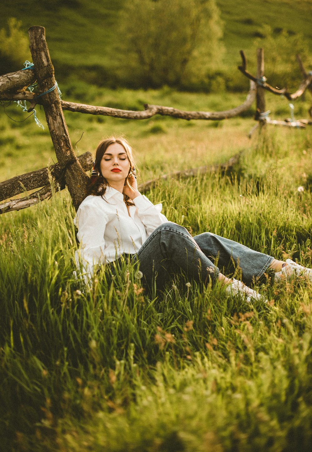 a woman sitting in a field with a fence in the background