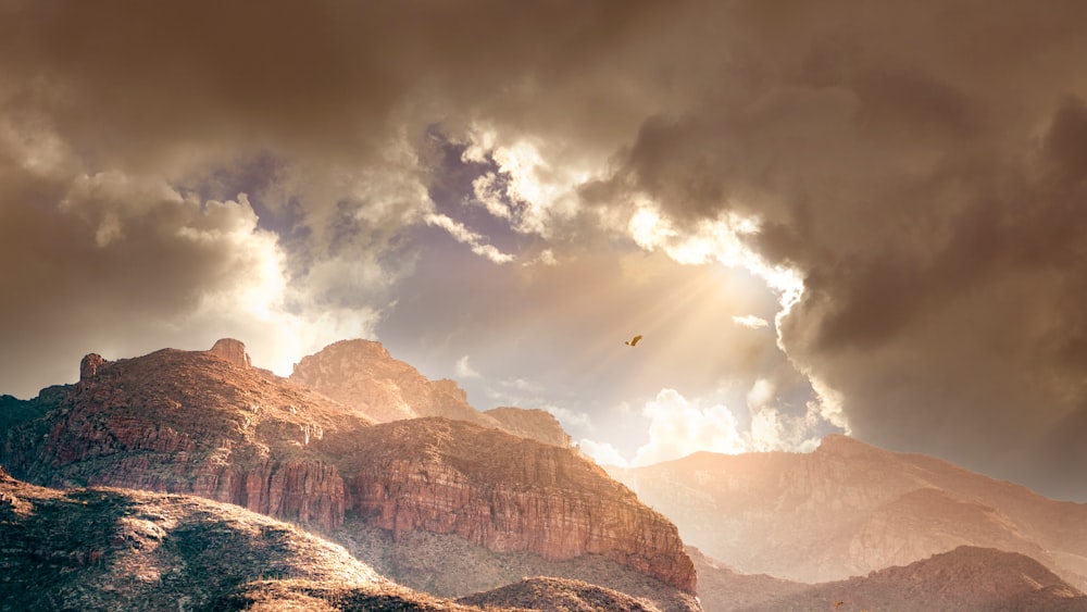 birds flying over brown rocky mountain under white clouds during daytime