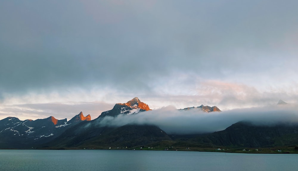 snow covered mountain near body of water under cloudy sky during daytime